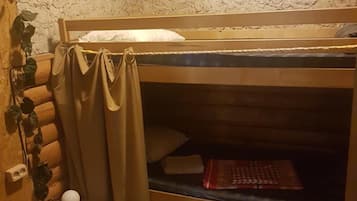 Ein Etagenbett mit Kopfteil, ein Nachttisch mit Schubladen, eine kleine Lampe und eine an der Wand befestigte Steckdose.