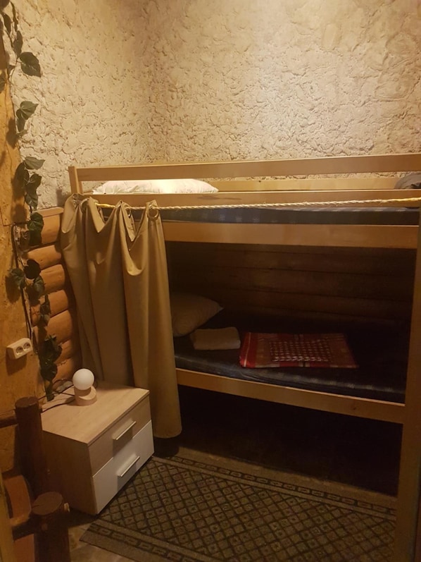 A bunk bed with a headboard, a bedside table with drawers, a small lamp, and a wall-mounted power outlet. - Hostel P33 (Tallinn)