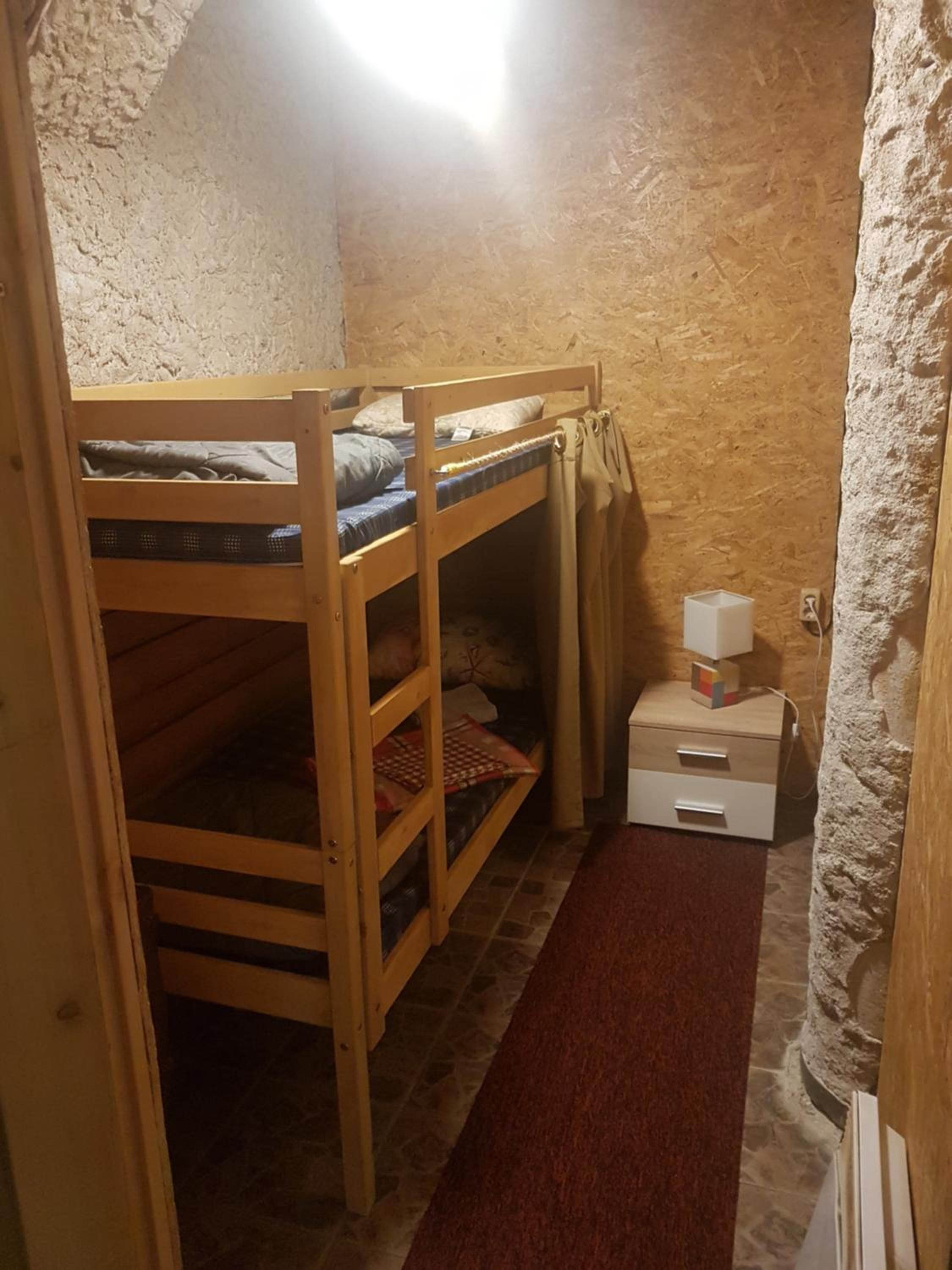 Ein kleines, rustikales Zimmer mit einem Etagenbett, einem Tisch mit einer Lampe und einem roten Teppich.