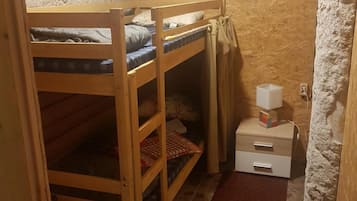 A small, rustic room with a bunk bed, a small table with a lamp, and a red carpet.