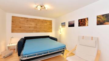 A bedroom with a bed, a chair, a wooden wall panel, and three pictures on the wall.