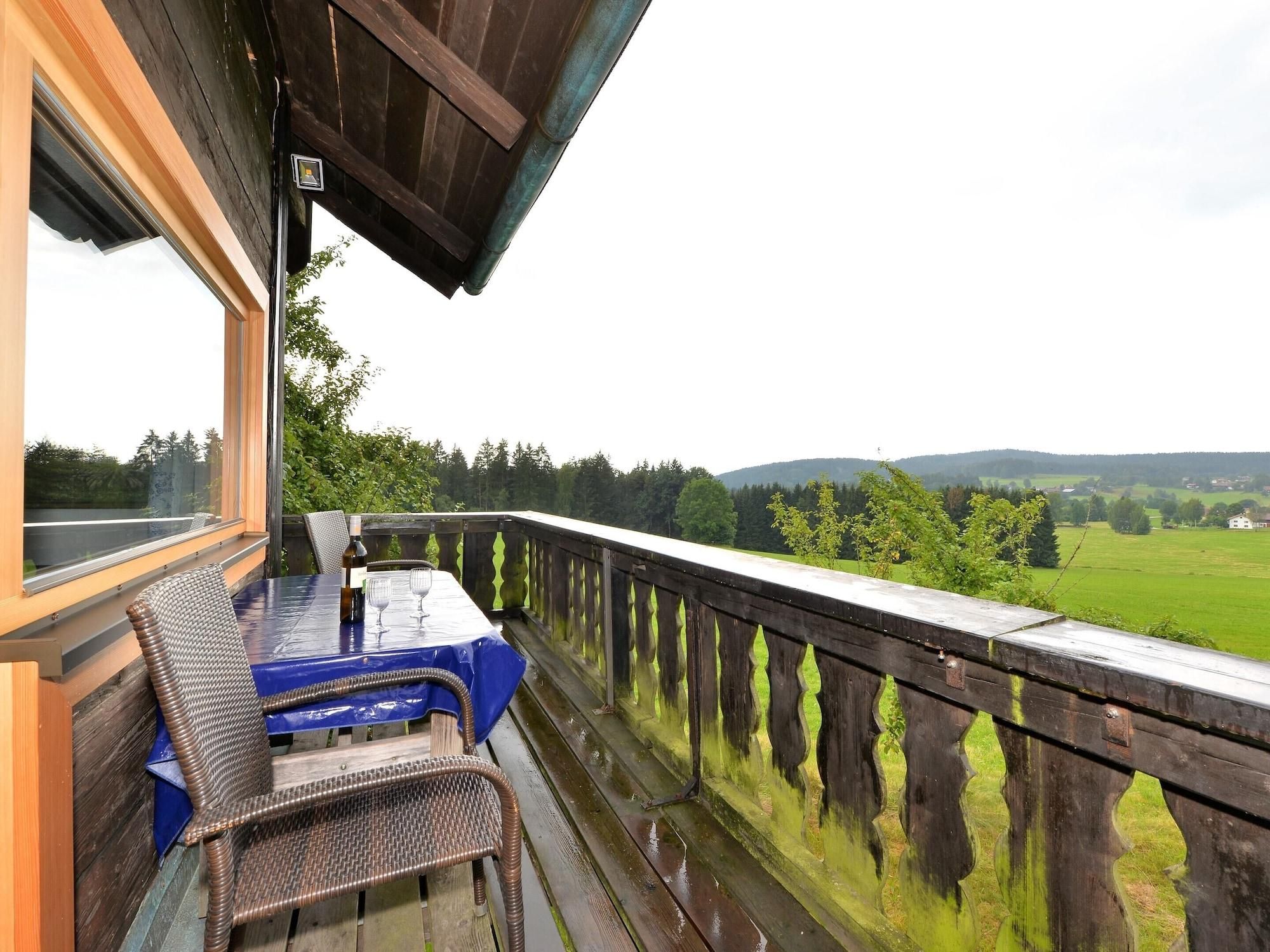 Une terrasse en bois avec une table et des chaises, donnant sur un paysage verdoyant.