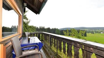 A wooden deck with a table and chairs, overlooking a green landscape.