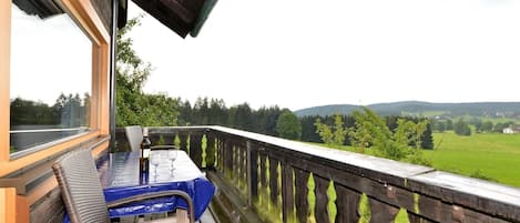 A wooden deck with a table and chairs, overlooking a green landscape.