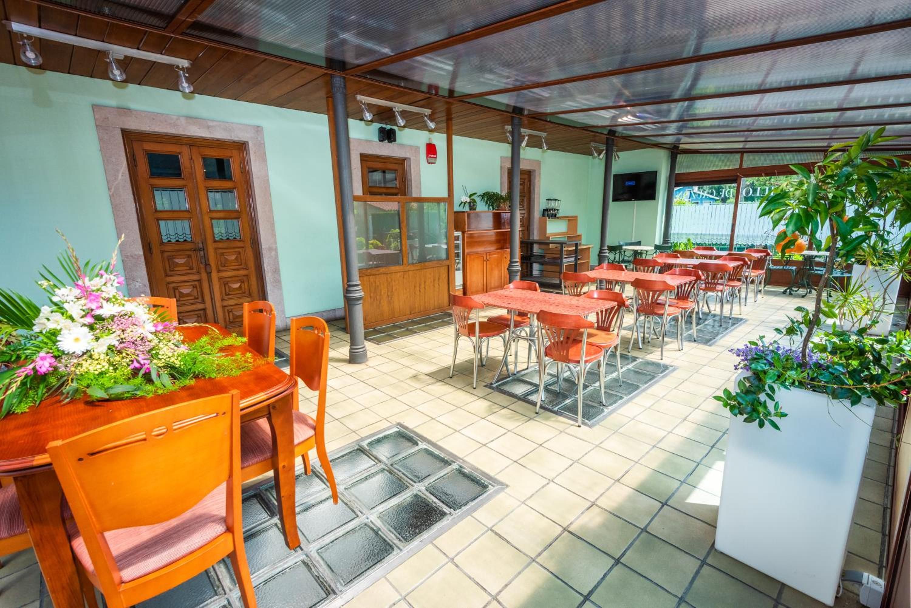 A restaurant with outdoor seating, wooden tables, and chairs, a tiled floor, and potted plants.