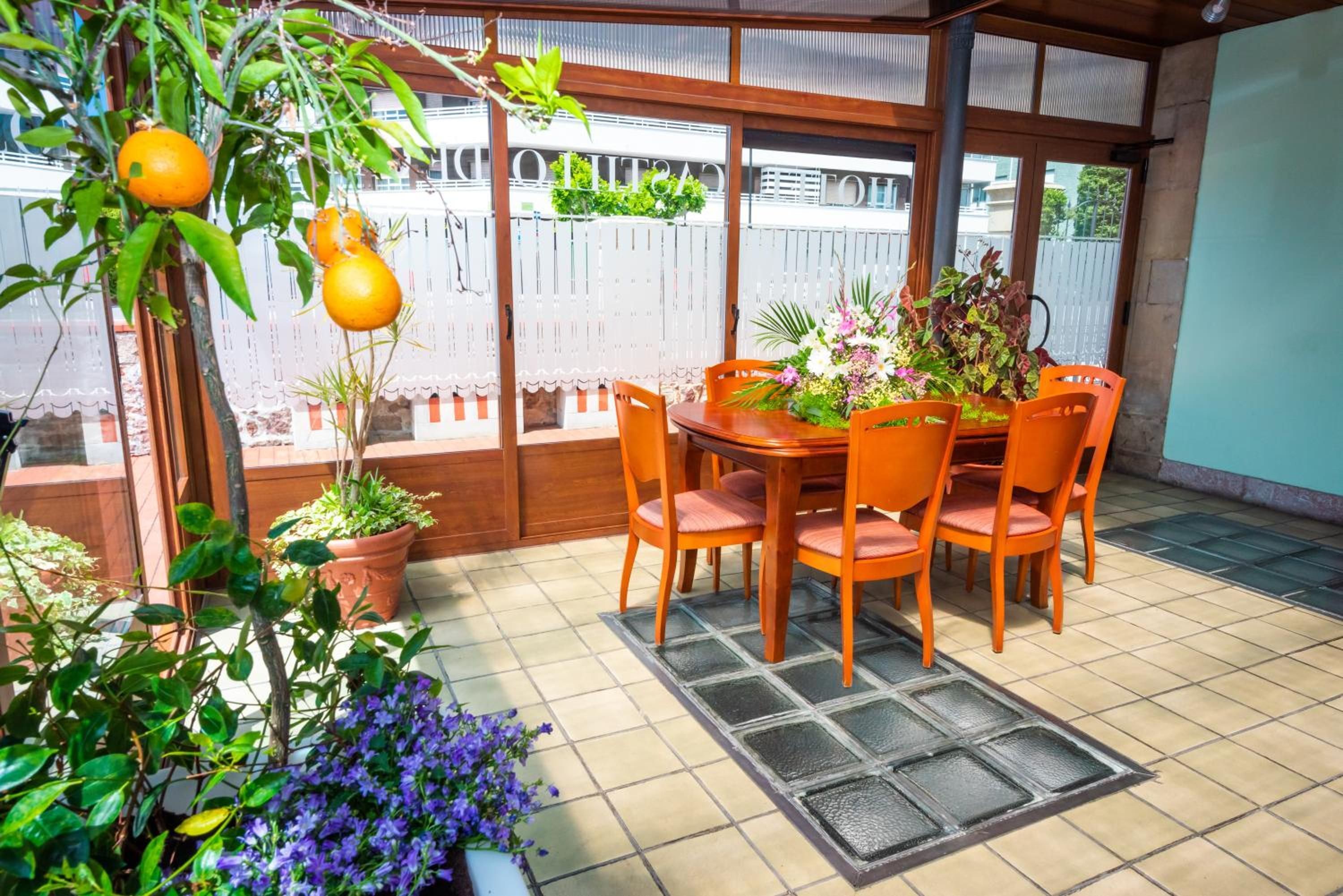 Un patio couvert avec une table et des chaises en bois, entouré de plantes en pot et offrant une vue sur un bâtiment en arrière-plan.