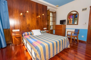 Una habitación de hotel con cabecera de madera, cama con colcha a rayas, escritorio con silla, televisión y espejo.
