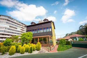 A multi-story building with a modern architectural design, featuring a mix of glass and wood elements, and a well-maintained garden with trimmed bushes. - Hotel Castillo De Gauzón (Castrillon)