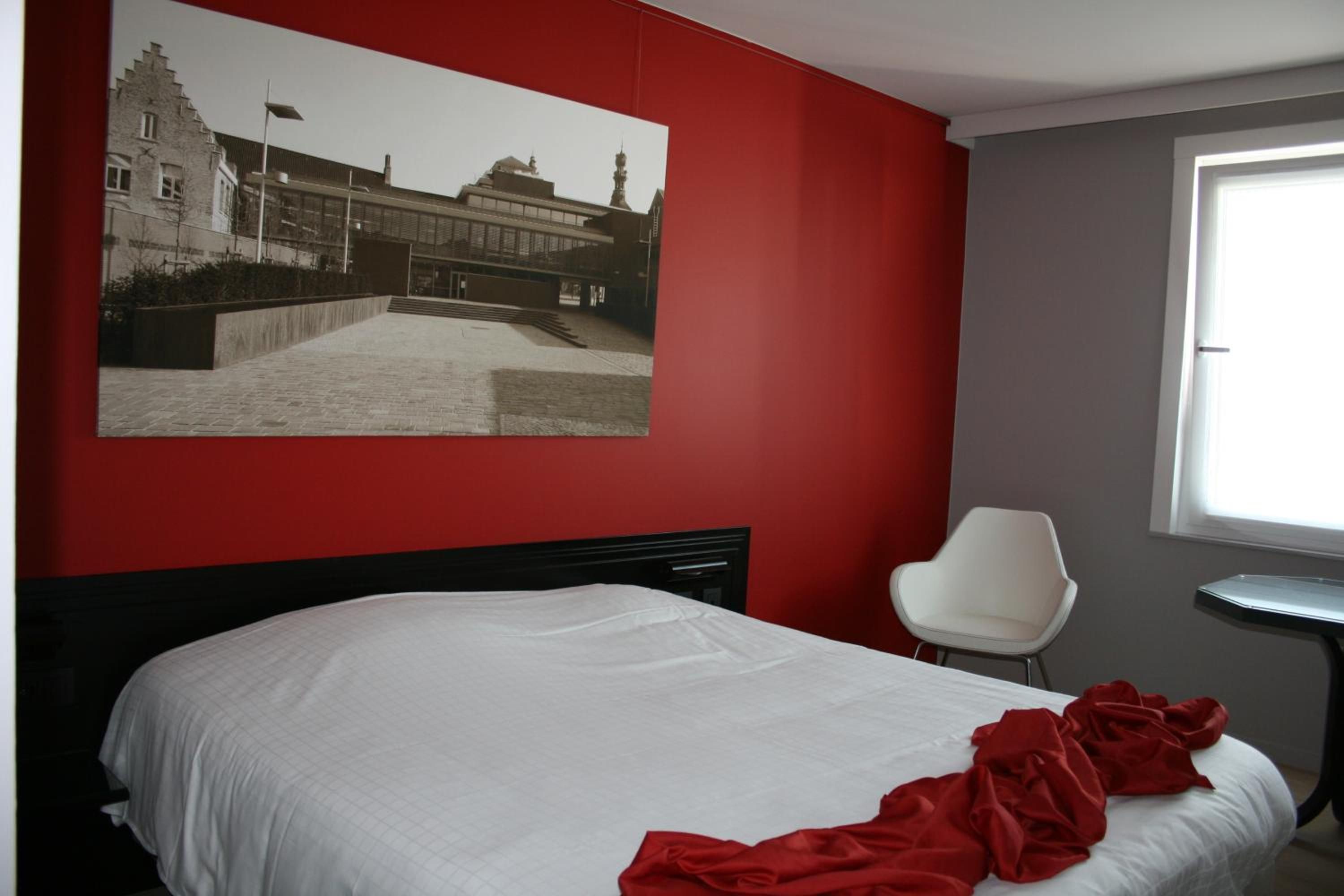 A hotel room with a large bed, a white chair, and a window.