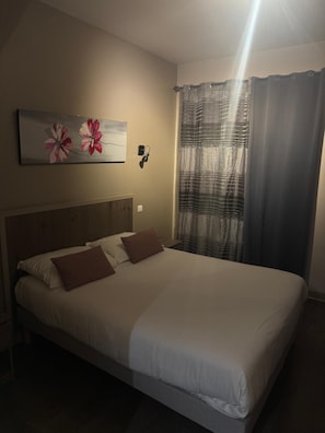 Quarto com cama, cabeceira, luminária na parede e um quadro.