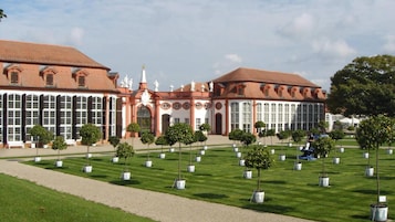 Un edificio grande con arquitectura simétrica, una entrada central con estatuas y un césped bien cuidado con árboles regularmente espaciados.