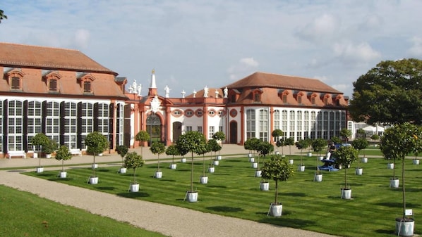 Un edificio grande con arquitectura simétrica, una entrada central con estatuas y un césped bien cuidado con árboles regularmente espaciados.