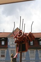 Varias salchichas colgadas en ganchos, con un edificio al fondo.