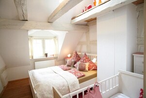 Un dormitorio con techo inclinado, cama con ropa de cama estampada, una ventana y un radiador.