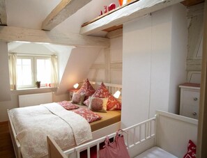 Un dormitorio con techo inclinado, una cama con ropa de cama estampada, una mesita de noche con lámpara y una ventana con cortinas.