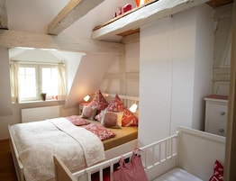 Un dormitorio con techo inclinado, una cama con ropa de cama estampada, una mesita de noche con lámpara y una ventana con cortinas.