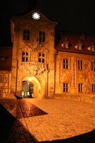 Un edificio histórico con una torre de reloj, fachada ornamentada y un patio adoquinado.