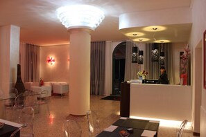 A hotel lobby with a reception desk, seating area, and a large chandelier. - Momi's Hotel (Cavarzere)