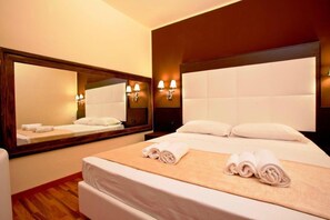 A hotel room with a large bed, a wooden headboard, a mirror, and wall-mounted lamps. - Momi's Hotel (Cavarzere)