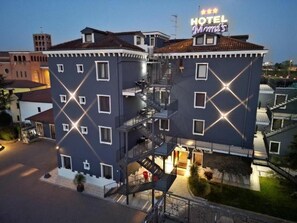 A multi-story hotel with a prominent staircase and a neon sign indicating it is a hotel. - Momi's Hotel (Cavarzere)