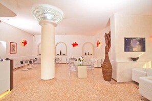 A modern interior with a central round table, clear chairs, a tall white column, and a large vase. - Momi's Hotel (Cavarzere)