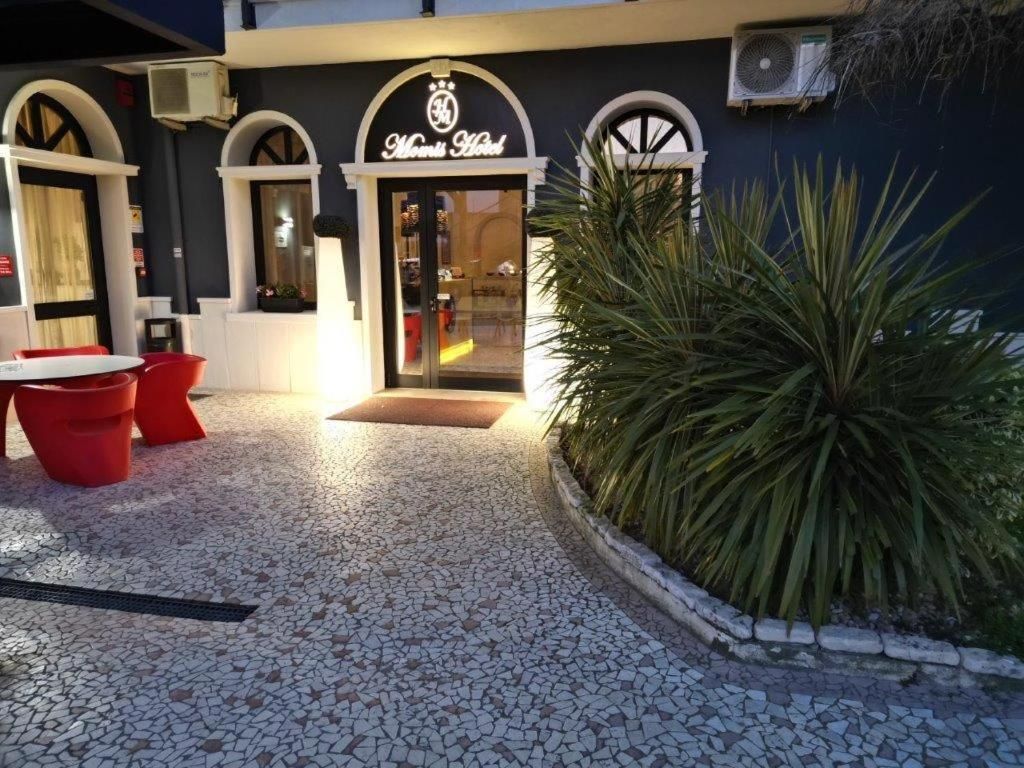 A hotel entrance with a tiled patio, red chairs, and a large plant.