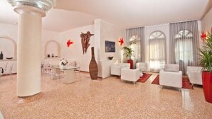 A spacious hotel lobby with a central seating area, a reception desk, and a large pillar. - Momi's Hotel (Cavarzere)