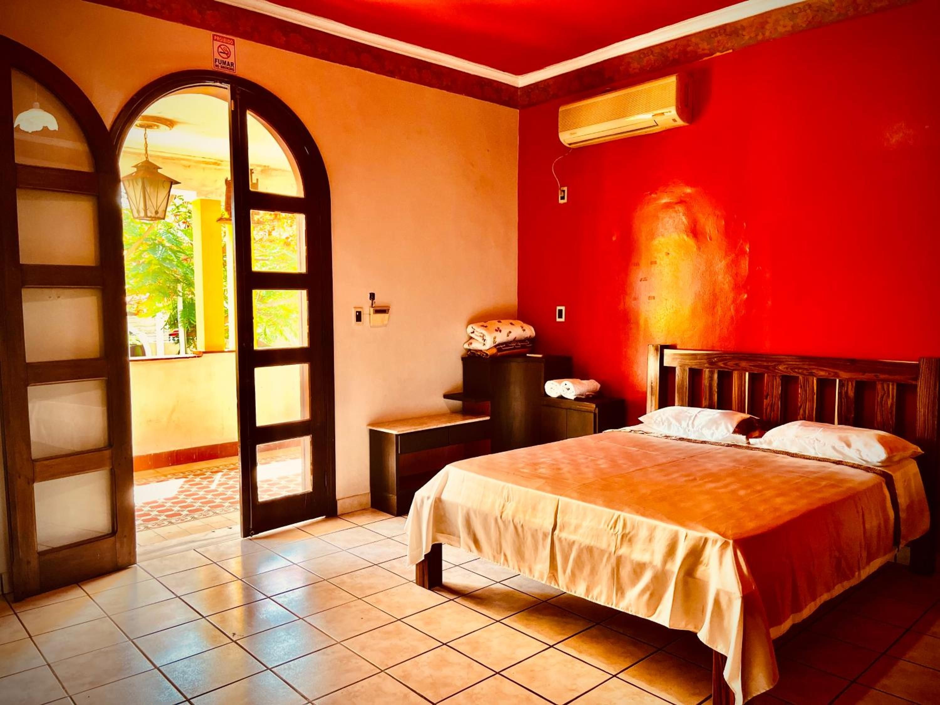 Quarto com cama, mesa de cabeceira, ar condicionado fixado na parede e porta aberta para uma varanda.
