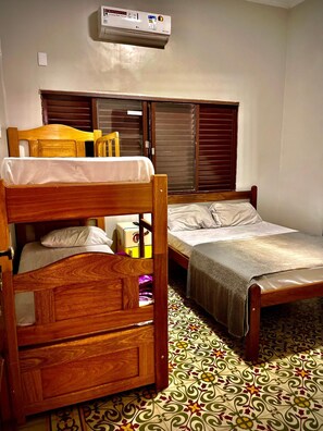 Una habitación con dos camas literas de madera, una mesita de noche pequeña, una silla y una ventana con persianas.