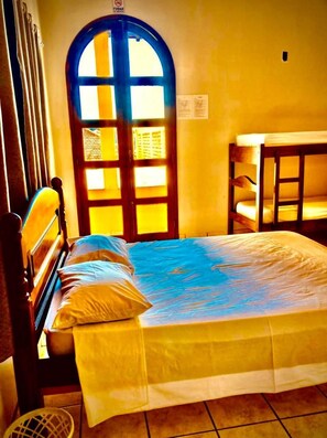 A room with a bed, a wooden chair, a small table, and a door with a window.