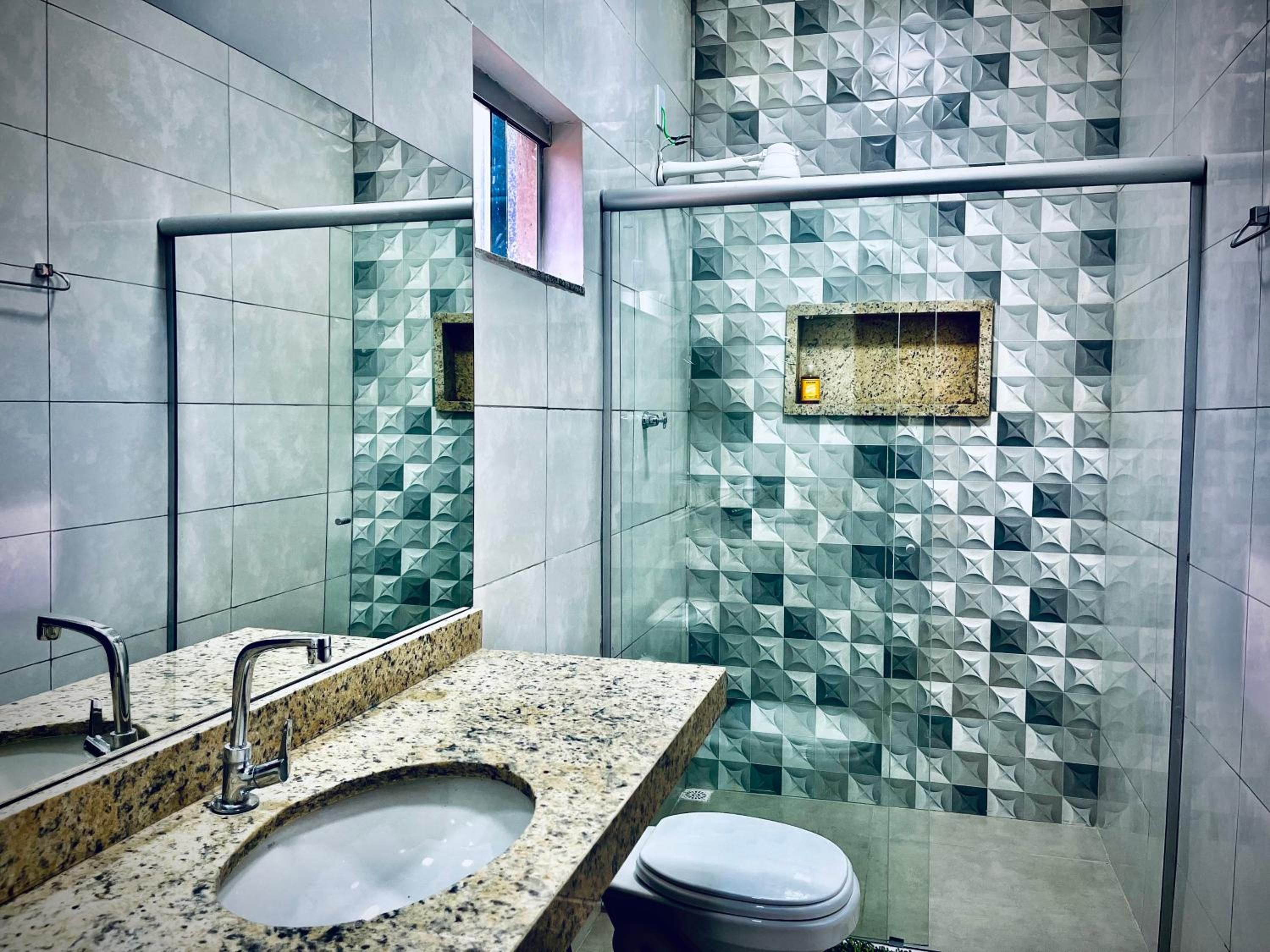 A modern bathroom with a granite sink, a mirror, and a glass shower enclosure with geometric tile patterns.