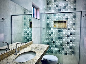 A modern bathroom with a granite sink, a mirror, and a glass shower enclosure with geometric tile patterns.