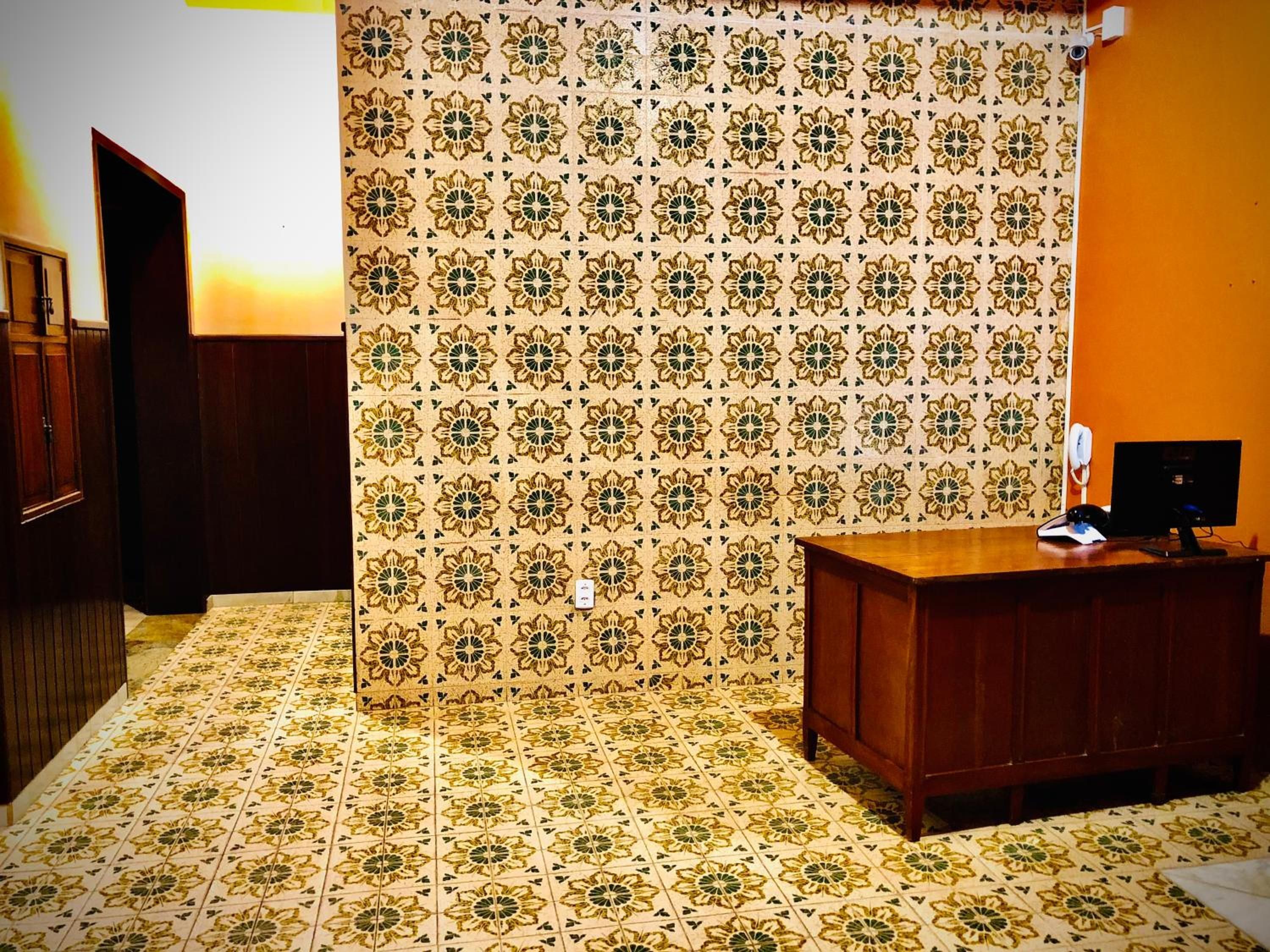 Quarto com papel de parede estampado, uma escrivaninha de madeira e um telefone.