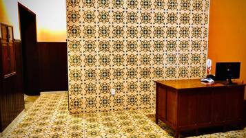 Quarto com papel de parede estampado, uma escrivaninha de madeira e um telefone.
