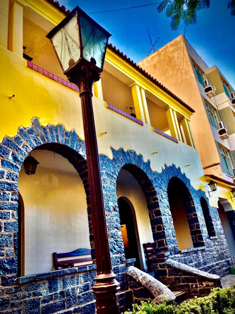 Um edifício com fachada amarela, arcos com padrão azul e um poste de luz.