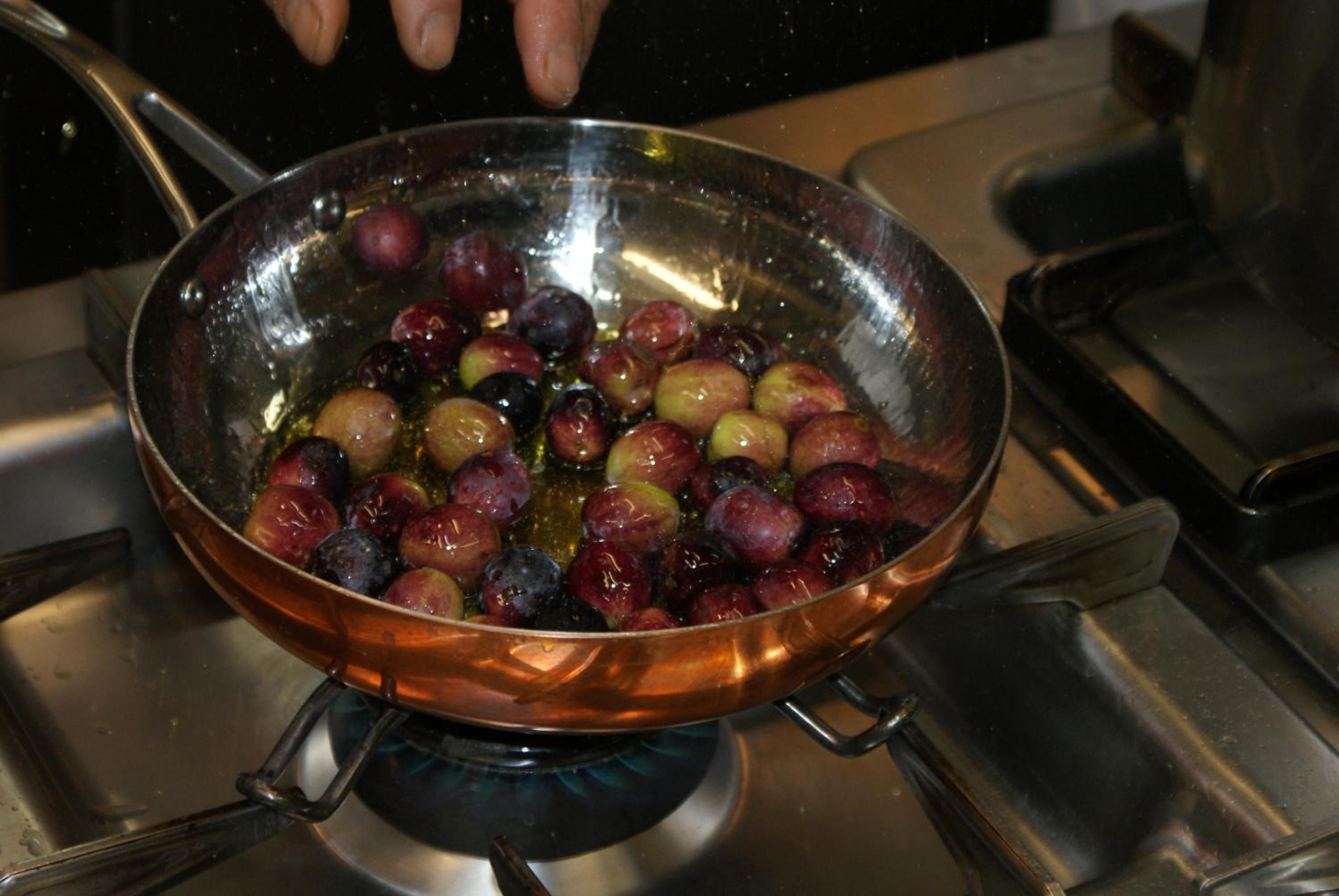 A copper pan on a stove with a mixture of red and green fruits being cooked.
