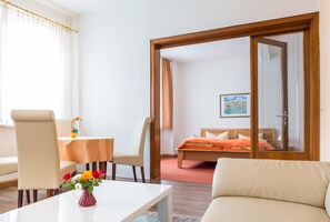 A hotel room with a bed, a sofa, a dining table with chairs, and a small table with a vase of flowers.