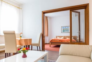 Quarto de hotel com uma cama, um sofá, uma mesa de jantar com cadeiras e uma pequena mesa com um vaso de flores.
