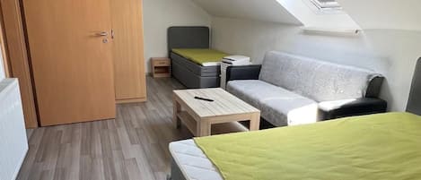A compact, modern room with a sloped ceiling, a bed, a sofa, a small table, and a wardrobe.