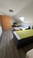 A compact, modern room with a sloped ceiling, a bed, a sofa, a small table, and a wardrobe.