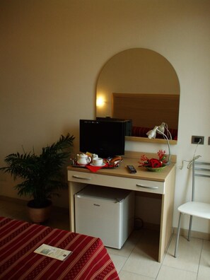 A hotel room with a desk, a television, a small refrigerator, a potted plant, a bed with a red and white striped bedspread, and a white chair.