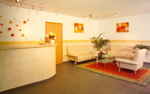 Ein Empfangsbereich mit einer Rezeption, einer Couch, einem Couchtisch und zwei Bildern an der Wand.