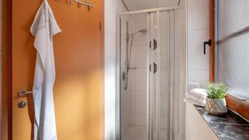 Ein Badezimmer mit Duschkabine aus Glas, einem Handtuchhalter und einer Topfpflanze auf der Ablagefläche.