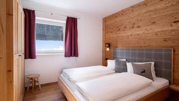 Ein Schlafzimmer mit zwei Betten, Holzwänden, einem kleinen Hocker und einem Fenster mit Vorhängen.