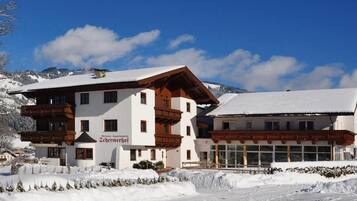 Ein zweistöckiges Hotel im traditionellen alpinen Baustil, mit hölzernen Balkonen und einer schneebedeckten Landschaft.