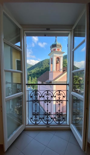 A balcony with a wrought iron railing, a view of a church with a bell tower, and a mountainous landscape. - Ostello Voltaggio (Voltaggio)