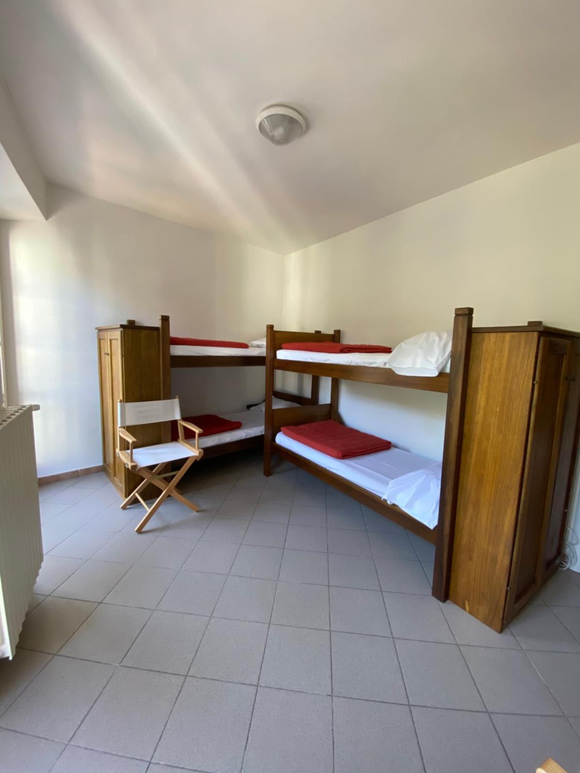 Una camera del dormitorio con letti a castello, una sedia pieghevole e una luce a soffitto.