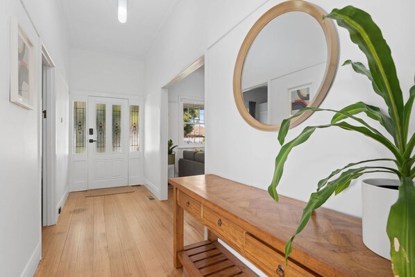 A hallway with a wooden bench, a round mirror, and a potted plant.