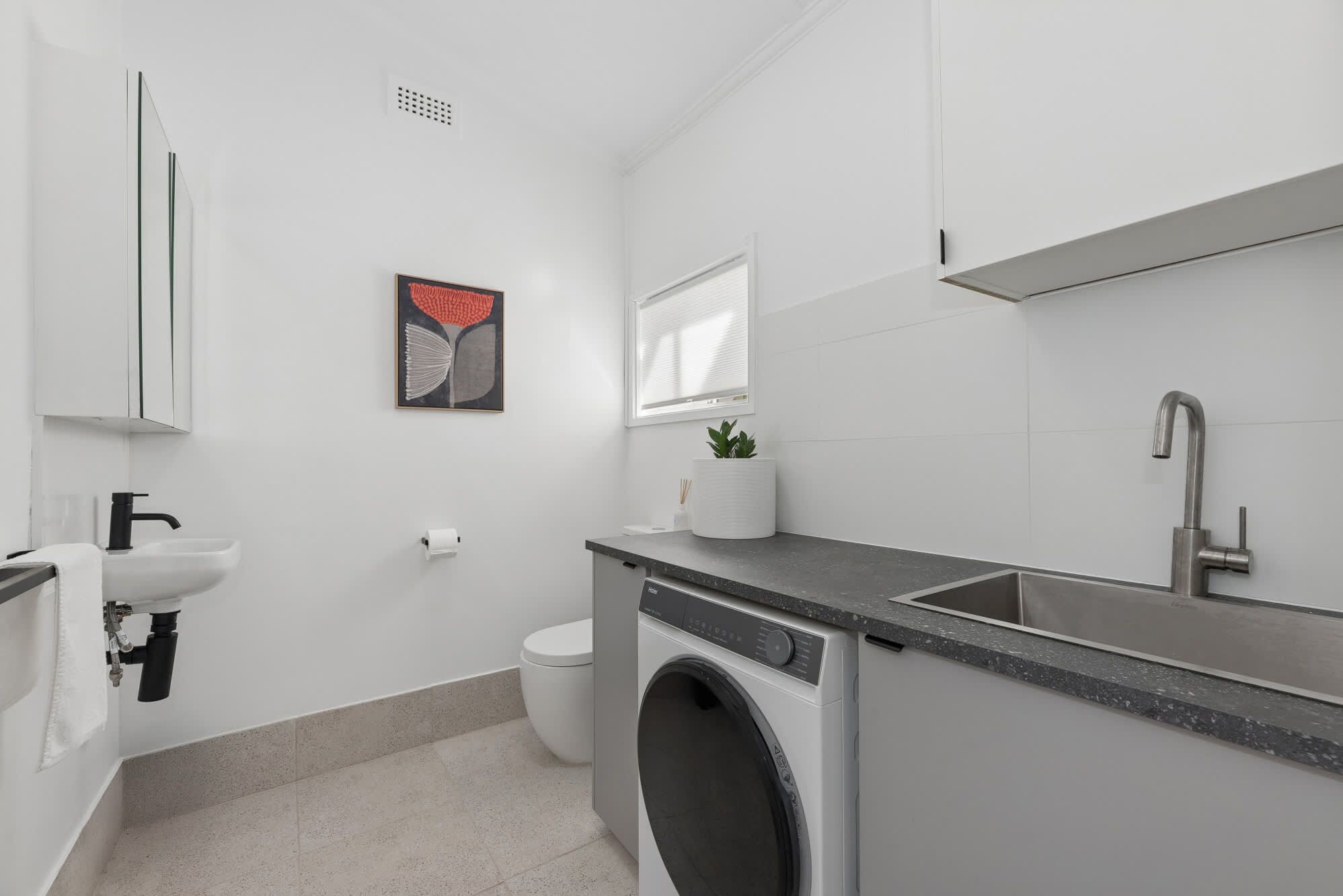 A modern bathroom with a washing machine, sink, and toilet.