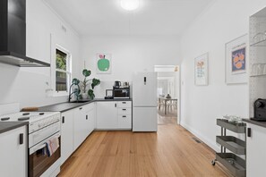 A modern kitchen with white cabinetry, a stainless steel range hood, a built-in oven, and a microwave. There is a dining area visible in the background.